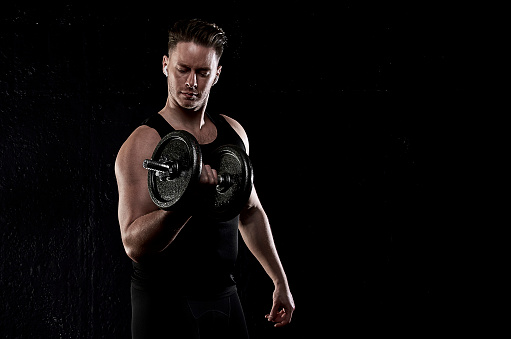 White young athletic man exercising with weights wearing ear pods
