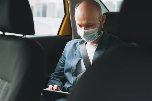 bald man businessman in medical face mask using tablet mobile phone inside yellow car taxi, concept of coronavirus quarantine - illness mask pollution car imagens e fotografias de stock