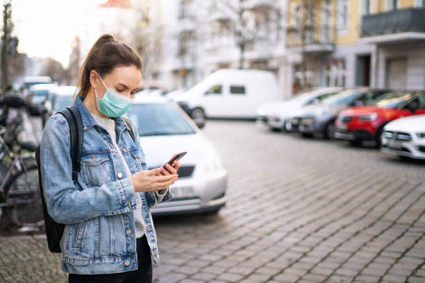 woman wearing a medical mask and using a phone outdoors - illness mask pollution car imagens e fotografias de stock