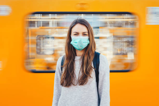 Woman wearing a medical mask in a subway Woman wearing a surgical mask standing in front of the moving train standing on subway platform stock pictures, royalty-free photos & images