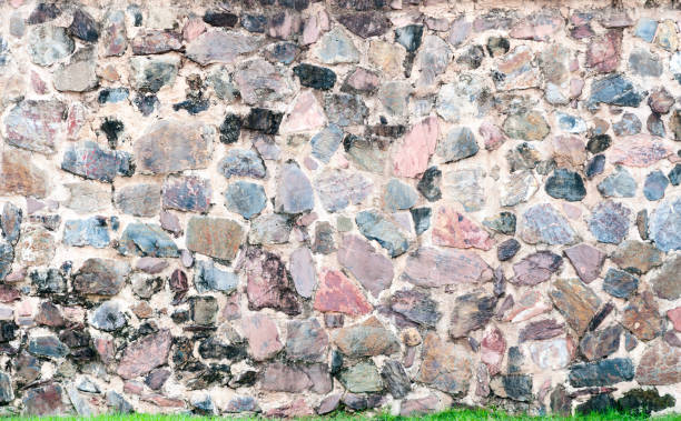 istock pattern decorative uneven cracked real stone wall surface with cement and green grass 1216169848