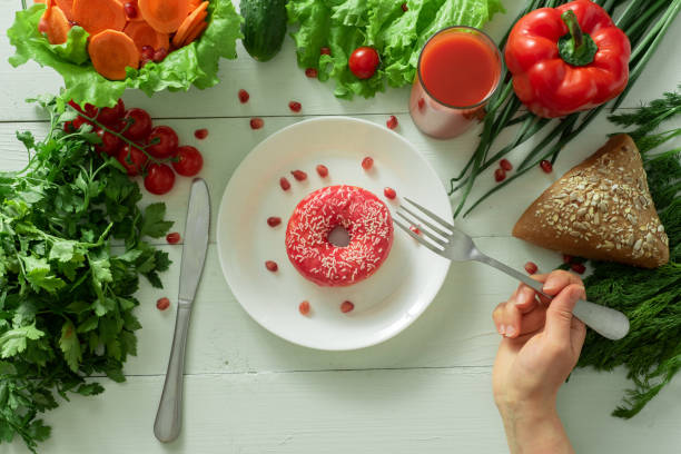 A delicious donut lies on a plate and eats to eat it. Problems of proper nutrition and the concept of choosing between wholesome and not wholesome food