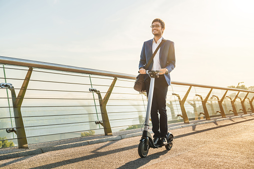 Concepto de transporte ecológico. Joven hombre de negocios en traje montando scooter eléctrico en la oficina photo
