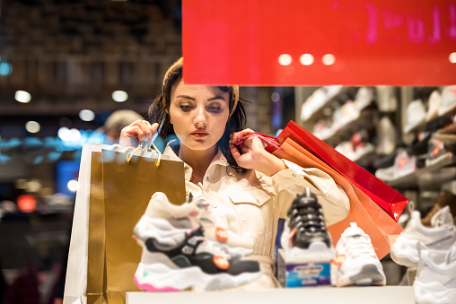 Beautiful woman in fashionable clothes looks different kind of sport shoes while shopping in store with bags.Shopping, lifestyle concept