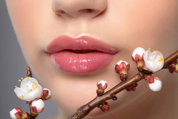 giovane ragazza con bella nude make-up e labbra paffute. labbra naturali perfette si chiudono. vicino a lei sono bellissimi fiori sakura primavera fioritura. trucco professionale e cura della pelle cosmetologia. - lip balm immagine foto e immagini stock