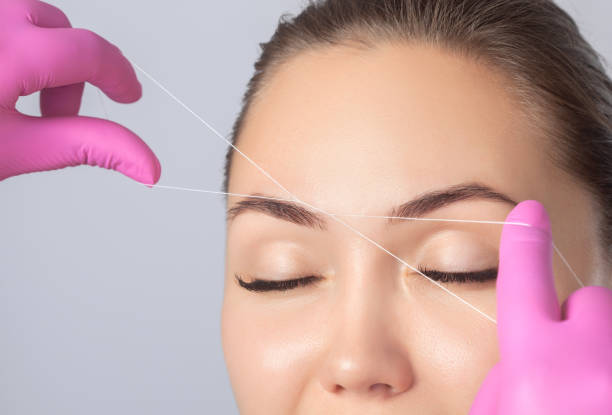 der make-up-künstler zupft augenbrauen mit einem faden nah. frauenkosmetik im schönheitssalon. - removing tweezing eyebrows eyebrow caucasian stock-fotos und bilder