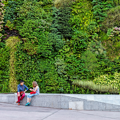 Madrid, Spain - 18 July 2018: Young Couple sitting near caixaforum. Caixaforum famous with green vertical garden. Madrid streets. City center of Madrid