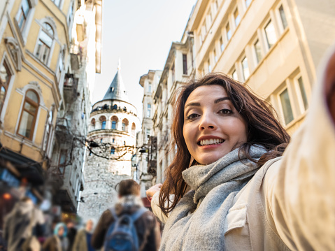 Beautiful young girl in fashionable clothes has selfie with view of landmark Galata tower in Beyoglu,Istanbul,Turkey