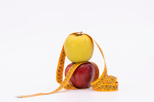 yellow and red apple with measure tape as symbol for diet and weight control