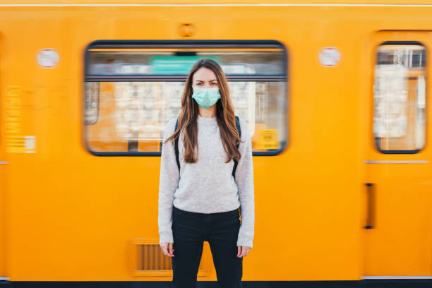 Woman wearing a medical mask in a subway Woman wearing a surgical mask standing in front of the moving train standing on subway platform stock pictures, royalty-free photos & images