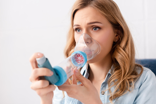 selective focus of asthmatic woman using inhaler with spacer