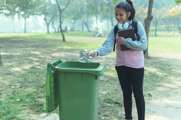 Indian young girl putting garbage in trash box. outdoor shoot in nature. girl cleaning to park. copy space.