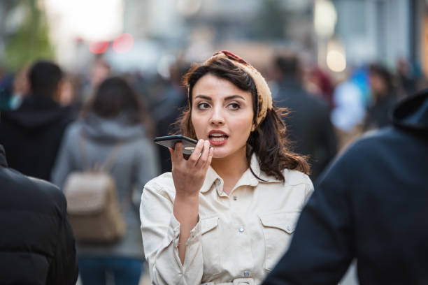 Beautiful young woman uses her smartphone voice recognition at street stock photo