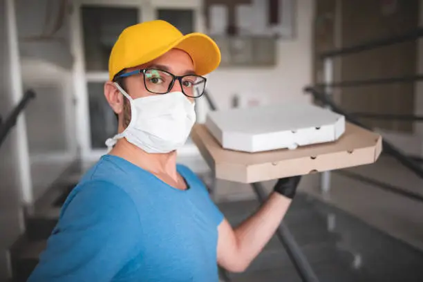 Deliveryman with protective medical mask holding pizza box - days of viruses and pandemic, food delivery to your home.