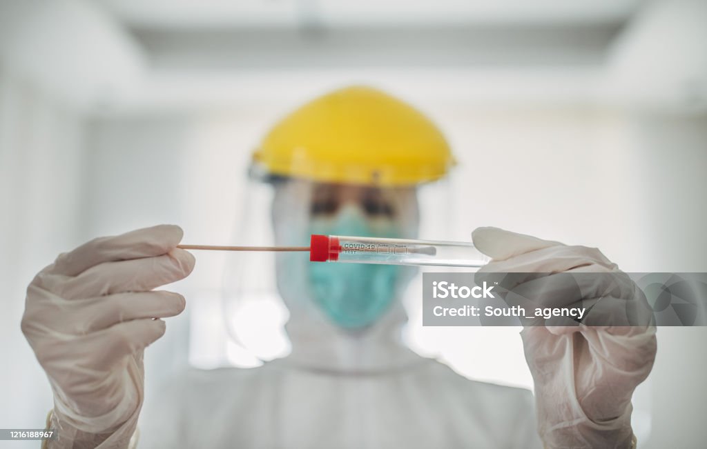 Doctor showing covid-19 tube test and sampling swab On woman, female doctor in protective suit holding and showing covid-19 tube test and sampling swab. Coronavirus Stock Photo