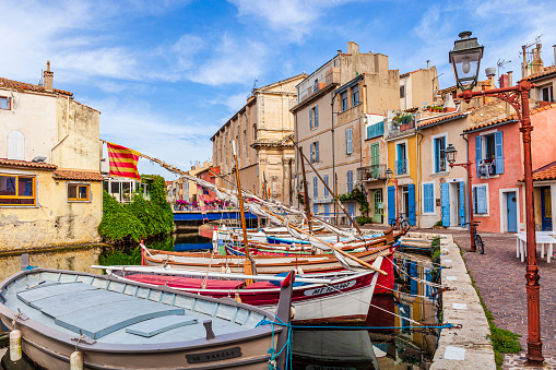 Colorful fishing boats moored at the harbor in the old town of Martigues, bordered by old pastel-colored buildings.