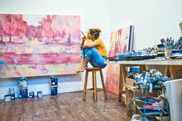 There's subtle beauty in every stroke Shot of a young woman sitting on a stool while looking at a painting in an art studio art class photos stock pictures, royalty-free photos & images