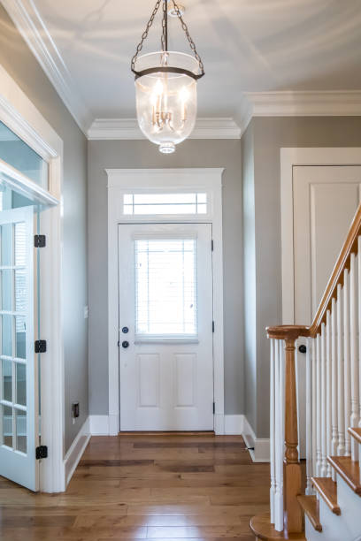 view of the interior front door from a hallway corridor entrance of a new construction house with hardwood floors, neutral gray walls and a hanging pendant style glass light chandelier - corridor entrance hall floor hardwood imagens e fotografias de stock