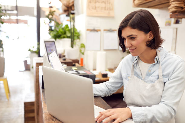 kobieta asystent sprzedaży pracy na laptopie za biurkiem sprzedaży kwiaciarni - clothing store sales clerk usa clothing zdjęcia i obrazy z banku zdjęć