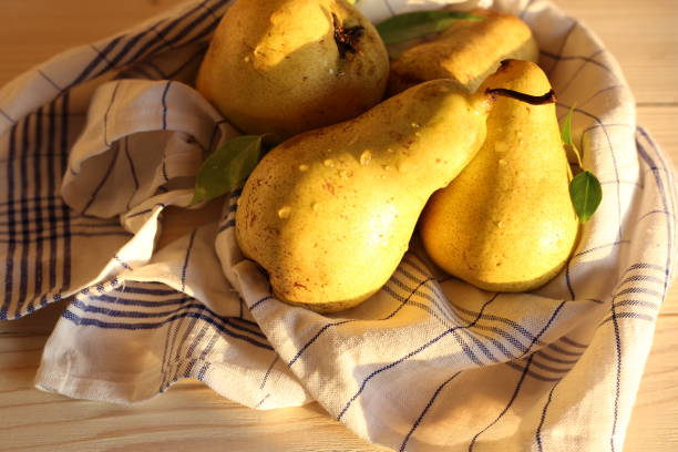 Real natural pears on a white wooden background with green leaves.  Sun fruits, pears on a  white table