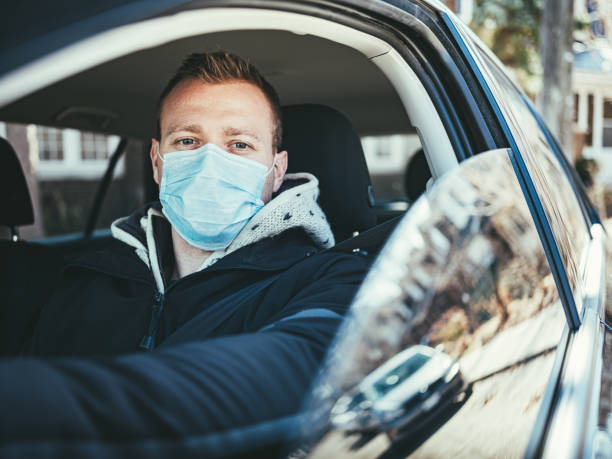 istock COVID-19, Young man wearing disposable face mask while driving 1216199608