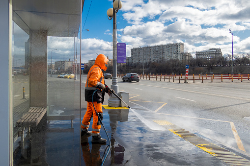 Moscow, Russia - February 29, 2020: Road worker cleaning city street with high pressure power washer, cleaning dirty public transport stops, Moscow, Russia