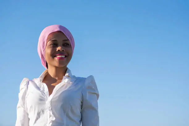 dark-skinned woman with a pink headscarf smiling