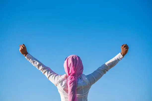 woman raising her arms with a pink headscarf and a white shirt