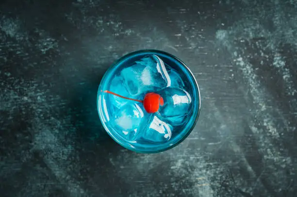 Photo of Blue old fashioned cocktail with cherry on the rustic background