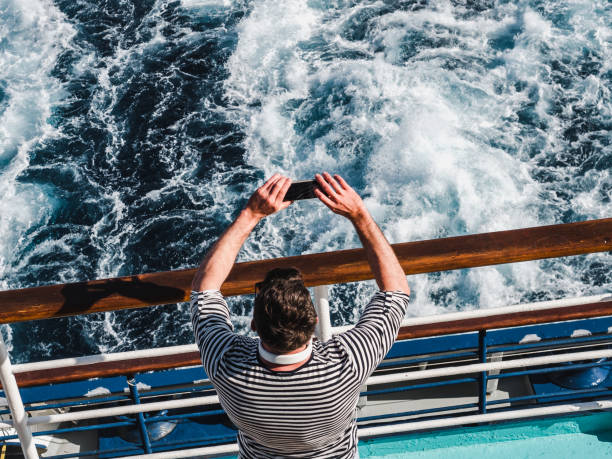 fashionable man holding a mobile phone on the deck - passenger ship sunset summer sun imagens e fotografias de stock