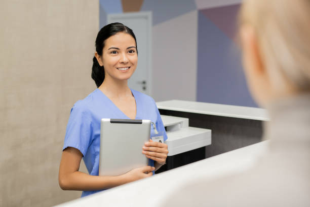 istock Cheerful young assistant or receptionist in blue uniform looking at patient 1216206707