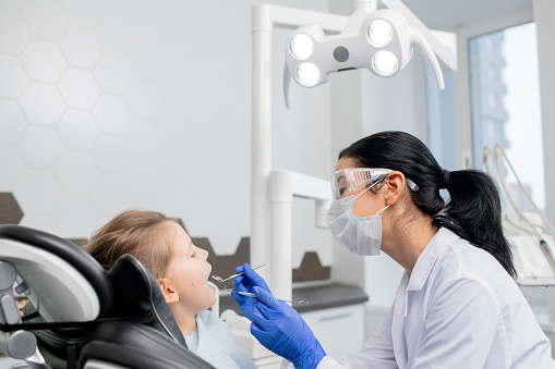 Joven odontóloga va a hacer chequeo oral de la cavidad oral de la pequeña paciente photo