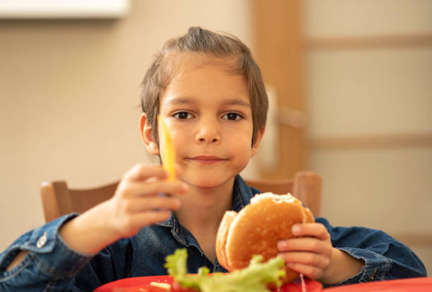 istock Little boy indoors eating a burger 1216211425