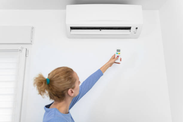 mujer sosteniendo un control remoto de una unidad de aire acondicionado moderna en casa. - pushing women wall people fotografías e imágenes de stock