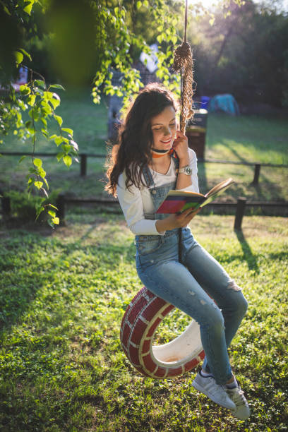 young woman playing on a swing and reading a book - freedom tire swing tire swing imagens e fotografias de stock