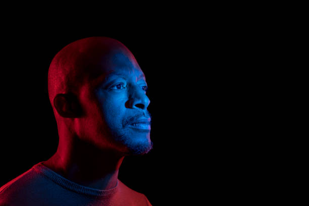 istock Black man with blue and red light, isolated on black background, looking sideways. 1216216317