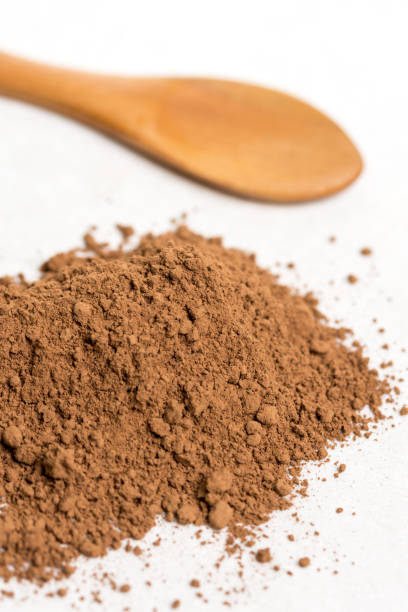 istock Brown cocoa powder with wooden spoon isolated above white marble background 1216219021