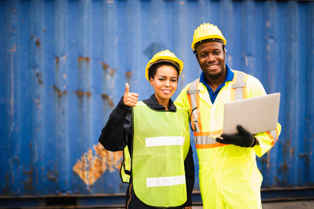 istock Young African american men and woman worker Check and control loading freight Containers by use computer laptop at commercial shipping dock felling happy. Cargo freight ship import export concept 1216219600
