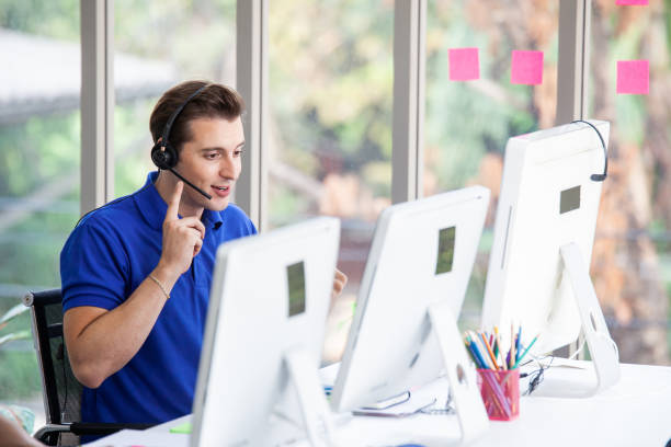 istock Young handsome male customer support phone operator with headset working in call center. Handsome male call center worker talking with a client and using computer in office 1216222433