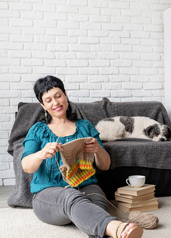 Stay home. Smiling middle aged woman enjoying being at home and knitting sitting on the sofa