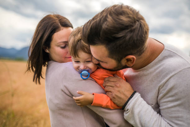 Young couple in a hug with their son in nature. Toddler with pacifier,walking in nature family with one child.
