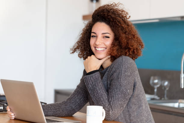 istock Smiling young woman working from home on laptop 1216225424