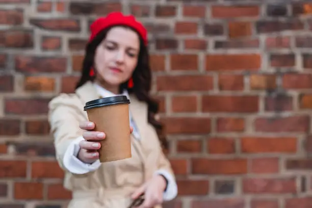 Close-up portrait of attractive pretty stylish cheerful curly-haired brunette girl holding at paper-cup coffee isolated on red brick background, Happy woman outdoors.