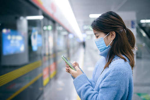Young Asian woman wearing a surgical mask and waiting for subway train at subway station.