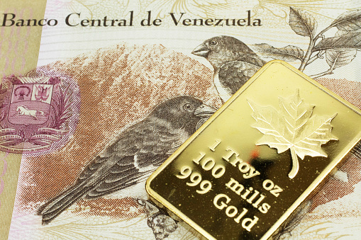 A macro image of a tan hundred Bolivar note from Venezuela with a gold bar.  Shot close up.