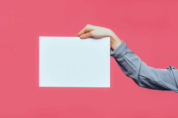 istock A hand holds a sheet with white paper on a pink background. Copy space. 1216233137