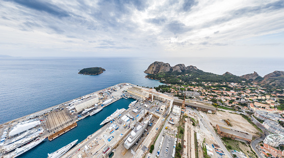 Aerial view of sea dry dock in La Ciotat city, France, the cargo crane, boats on repair, luxury sail yacht and motor yacht, mountain is on background, shipyard