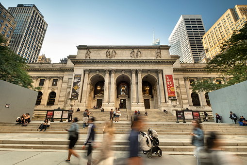Manhattan, New York - September 19, 2019:  A crowd of people walk on the sidewalk in front of the entrance to the New York public library next to Bryant Park in downtown Manhattan New York City USA