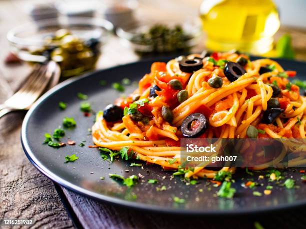 Pasta Puttanesca With Tomato Sauce Anchovies Chilli Capers And Olives On Wooden Table Stock Photo - Download Image Now