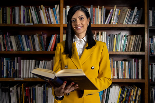 Portrait of a young beautiful woman in yellow suit at her workplace in the library